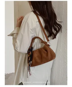 Détail de sac bandoulière en suède marron montrant la poignée nouée et le pompon.