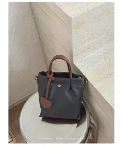 Sac seau minimaliste en nylon avec poignees en cuir marron et pendentif coeur elegant.