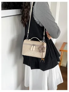 Detailed view of beige woven lunch box bag with shoulder strap and floral charm on model.
