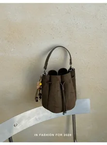 Detailansicht der eleganten braunen Wildleder Beuteltasche mit Kordelzug und Anhänger.