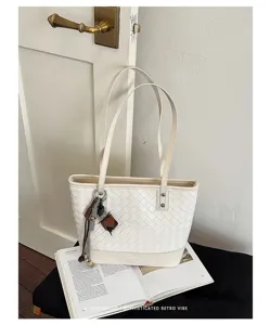 Gedetailleerd overzicht van witte geweven leren shopper met bedels op boek.