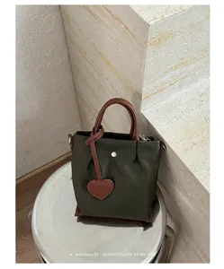Détail de sac seau en nylon, tissu vert et anses en cuir marron, style rétro minimaliste.