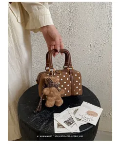 Detailed shot of retro brown polka dot Boston bag with cute teddy bear keychain on black stool.