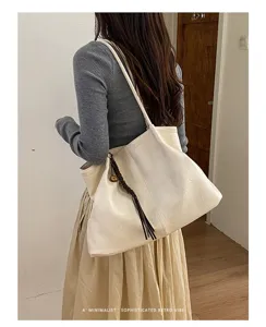 Vue détaillée du sac cabas souple beige minimaliste en cuir avec breloque pompon tressée.