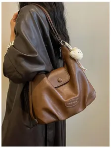 Dettaglio borsa a spalla retrò in pelle marrone con texture morbida e ciondolo chic.