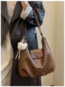 Dettaglio della borsa a spalla retrò in pelle marrone con un grazioso ciondolo in peluche.