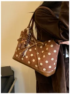 Close-up detail of brown polka dot shoulder bag with cute bow and bear plush charm.
