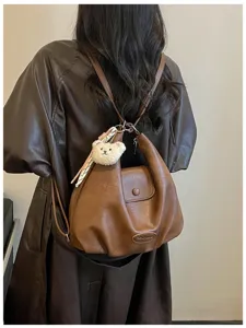 Dettaglio zaino retro in pelle marrone con ciondolo orsetto chic e tasca con patta.