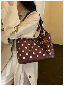 Detailed view of the brown polka dot underarm shoulder bag with bow and cute bear charm.