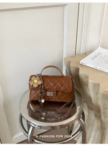 Detailed view of brown quilted chain shoulder bag with cute flower pendant on metal stool.