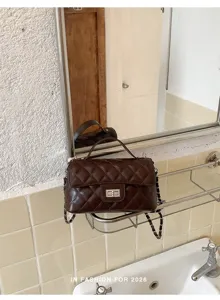 Close-up detail shot of the dark brown quilted chain shoulder bag resting on bathroom shelf.