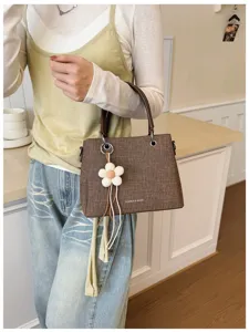 Primer plano de bolso de mano marrón texturizado para mujer con colgante de flor y asas.