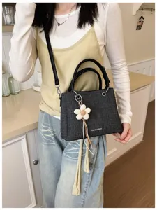Vista detallada de un bolso de mano de tela negra con colgante floral llevado por la modelo.