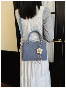 Detalle de un elegante bolso de hombro de tela azul con un bonito colgante de flor.