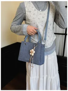 Bolso tote de mezclilla azul con correa y dije de flor, vista detallada de la textura y herrajes.