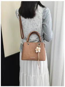 Vista detallada de bolso de mano tejido marrón, elegante bolso de hombro con colgante floral.