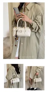 Close-up detail of white Boston handbag with metal buckle and beaded charm worn by model.