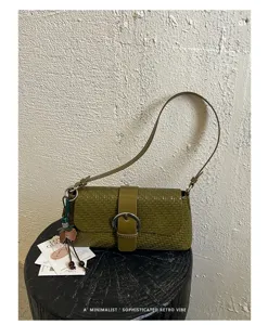 Detailed shot of olive green woven baguette shoulder bag with round buckle and charm.