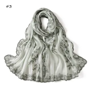 Detailed view of light green scarf with pine branch sequin embroidery and lace edge.