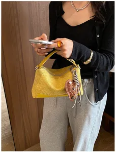Dettaglio della borsa a mano in pelle intrecciata gialla con ciondolo a cuore in stile retro.