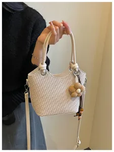 Détail de sac seau tissé exquis avec charme floral, design bandoulière élégant, finition beige.