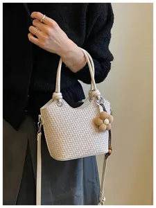 Vue détaillée du sac seau tressé avec charm fleur, mettant en valeur la texture et la poignée.