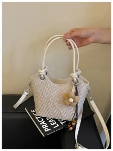 Gros-plan d'un sac seau tressé élégant en beige, orné d'un joli pendentif de fleur.