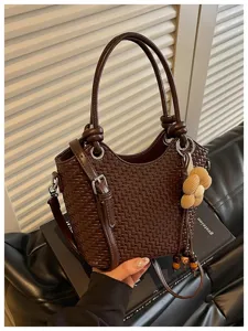 Détail de sac seau en cuir tressé marron foncé avec pendentif fleur chic et quincaillerie en métal.