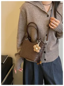 Gros plan sur le sac seau tressé marron doté d'un ravissant pendentif fleur et bandoulière.