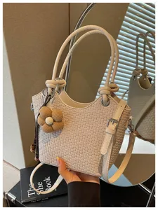 Détail de sac seau tissé beige montrant texture complexe, pendentif fleur et poignées.