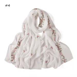 Detailed shot of delicate pink floral and bow embroidery on a lightweight white scarf.