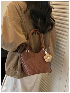 Détail de sac seau tressé marron chic avec cuir texturé et charmant pendentif floral mignon.