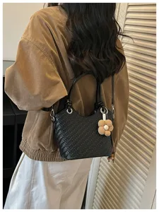 Vue de détail du sac seau noir tressé avec charmant pendentif fleur et bandoulière.