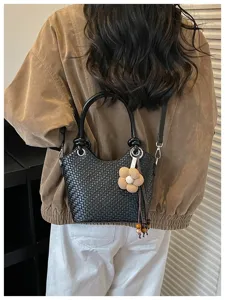 Vue de détail rapprochée du sac seau noir tressé porté au dos avec un charmant pendentif.