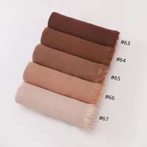 Gros plan de foulards unis roulés avec des extrémités frangées dans diverses nuances.