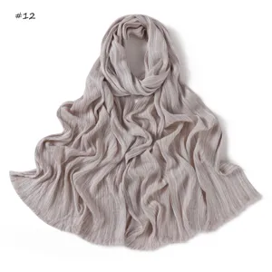 Detail view of the soft crinkled long scarf with frayed edges in light grey neutral tone.