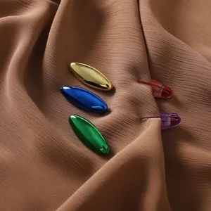 Vue de détail de boucles en plastique plates ovales métalliques colorées et broche épingle de sûreté.