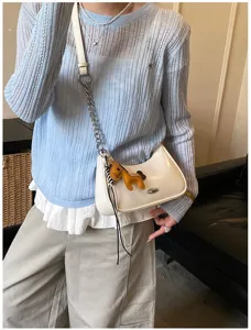 Primo piano di borsa a spalla in pelle bianca con ciondolo a cavallo giallo chic.