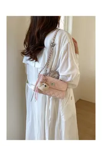 Detailed shot of a stylish pink quilted crossbody bag with chain strap and cute bear charm.