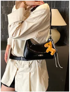 Dettaglio della borsa a spalla nera lucida con ciondolo a cavallo indossata dalla modella.