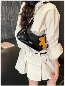 Dettaglio borsa a spalla in pelle verniciata nera, elegante borsa con catena e ciondolo cavallo