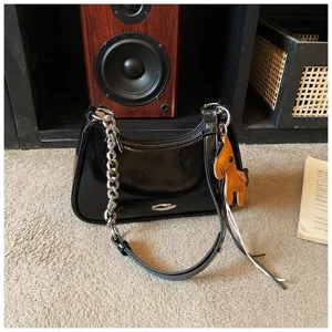 Primo piano della borsa a spalla in pelle verniciata nera con catena metallica e ciondolo.