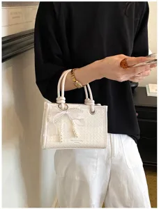 Detail van de witte geweven handtas met een elegante parel-strik-hanger voor dames.