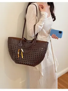 Dark brown woven leather tote bag detail with hollow cutout pattern and chic beaded charm.