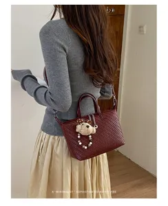 Stylish woven dumpling handbag detail showcasing retro burgundy texture and cute bear charm.