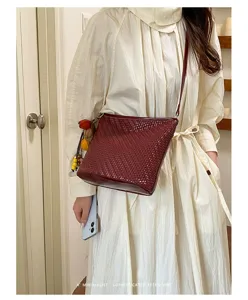Detailed view of a retro woven bucket bag in deep red, worn crossbody with charms for women.