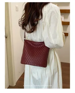 Burgundy woven leather bucket bag worn on shoulder, showing detailed texture and retro style.