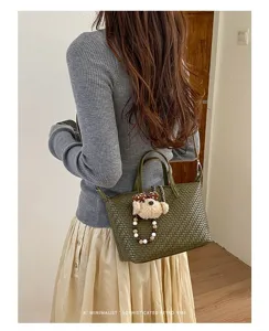 Green woven dumpling crossbody bag with cute plush bear charm for stylish daily commuting.