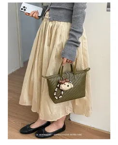 Stylish green woven dumpling bag for women, chic commuter handbag with cute plush charm decor.