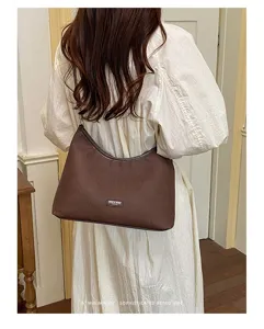 Detail shot of a minimalist brown shoulder hobo bag, retro style worn by a model indoors.